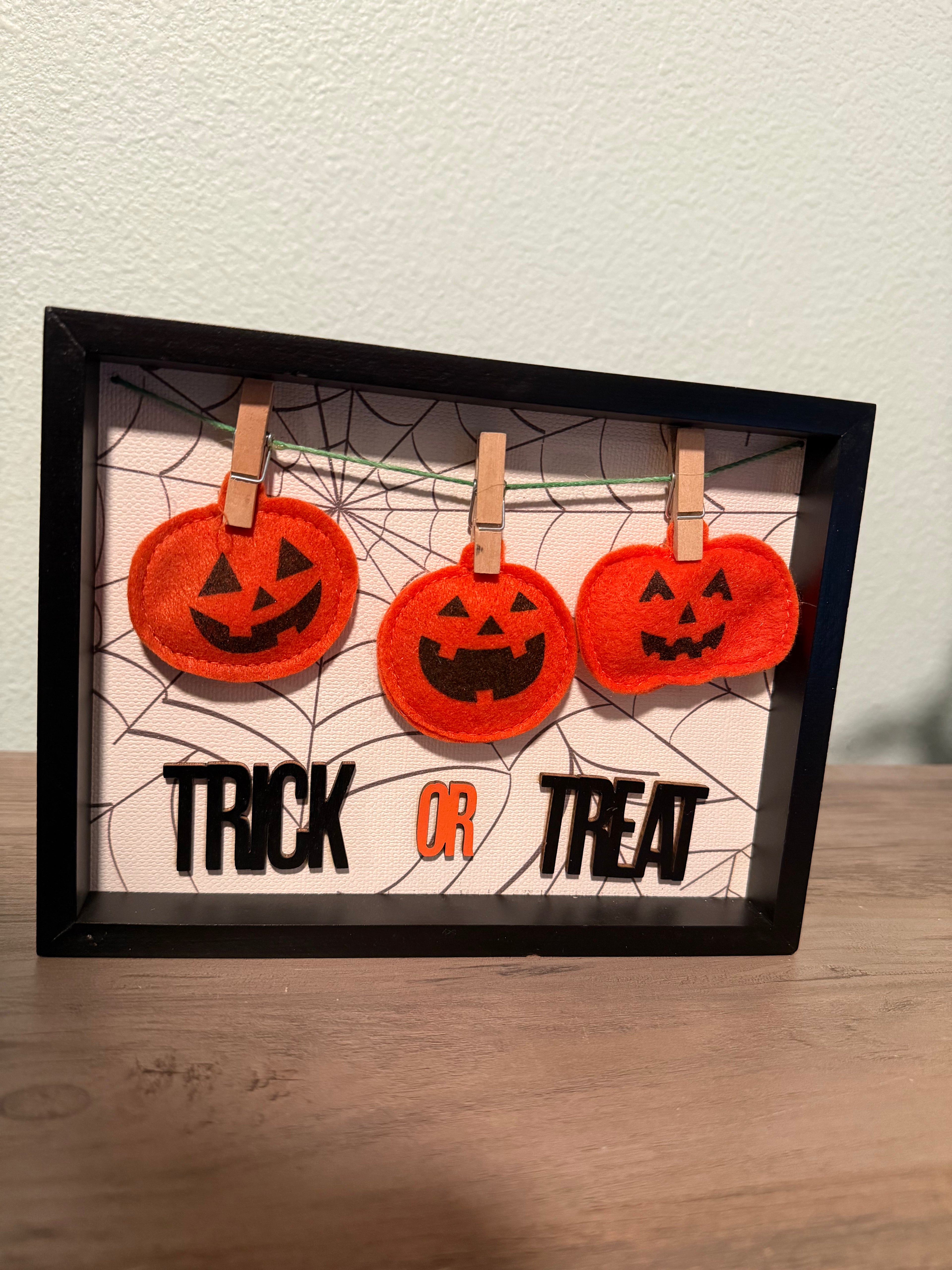 Halloween-themed framed art with jack-o'-lanterns and 'Trick or Treat' text on a spiderweb background.