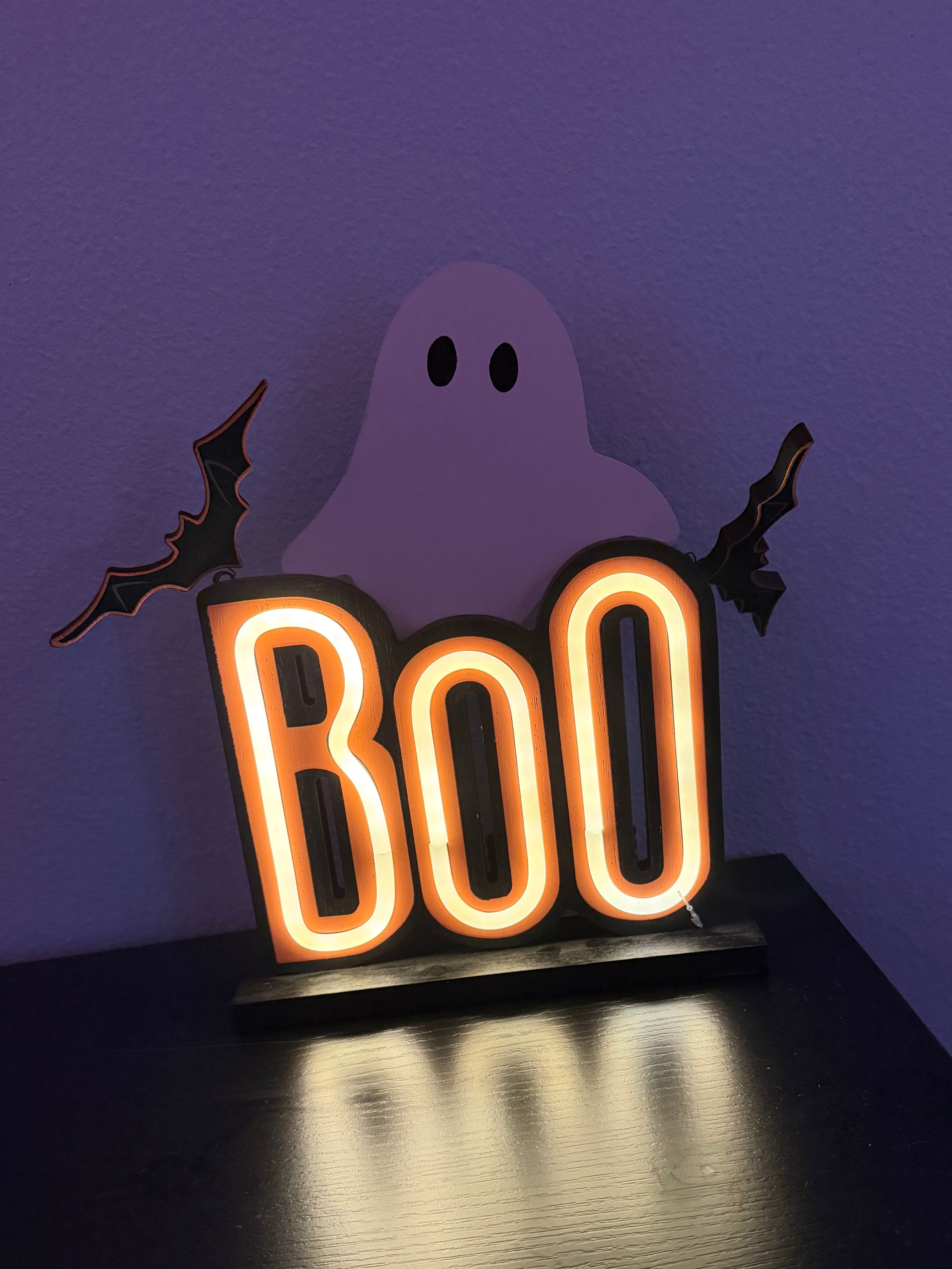 Neon 'BOO' sign with a ghost and bats on a purple background